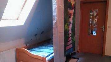 Ein Zimmer mit einem Einzelbett, einem Fenster mit Vorhang, einer Tür mit dekorativem Glasfeld und einem kleinen Teppich auf dem Boden.