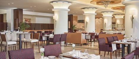 A spacious dining area with multiple tables and chairs, large pillars, and a chandelier.