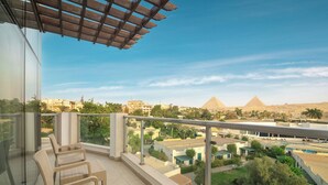 A balcony with wicker chairs, a glass railing, and a view of the pyramids. - Steigenberger Pyramids Cairo (Giza)