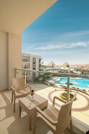 A balcony with wicker furniture, a view of a swimming pool, and pyramids in the background.