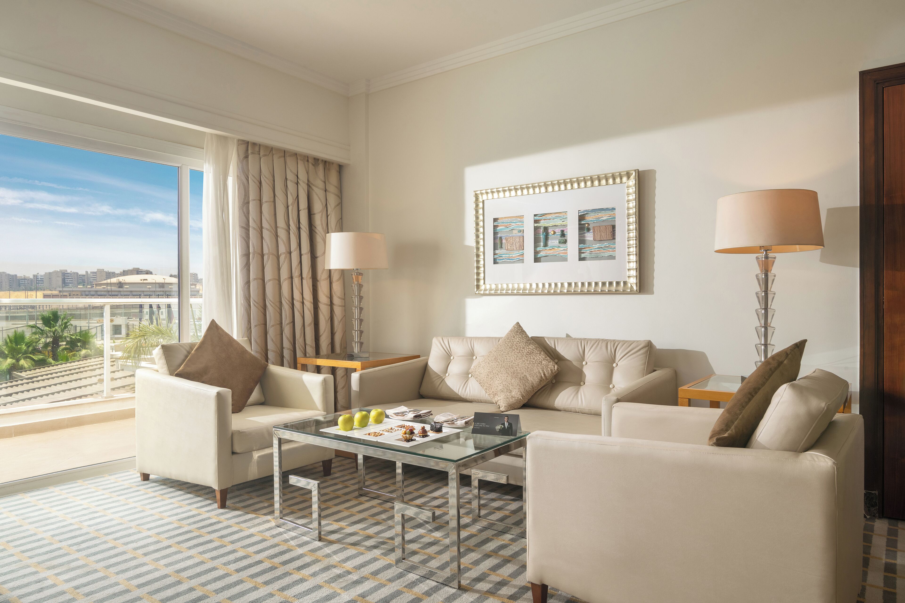 A modern hotel room with a large window, a sofa, a coffee table, and a lamp.