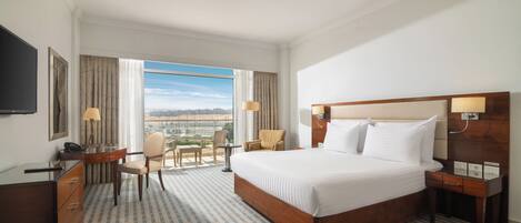 Habitación de hotel con una cama grande, un escritorio con silla, televisión y vista a la ciudad.