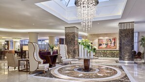 A spacious lobby with a high ceiling, a central chandelier, marble flooring, and a seating area with chairs and a table. - Steigenberger Pyramids Cairo (Giza)