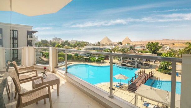A balcony with wicker furniture, a swimming pool, and views of pyramids. - Steigenberger Pyramids Cairo (Giza)
