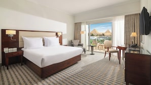 A hotel room with a large bed, a desk, a chair, and a view of the pyramids. - Steigenberger Pyramids Cairo (Giza)