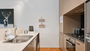 A modern kitchen with a stainless steel sink, a stove, and a refrigerator. There is a wooden floor and a painting of a deer on the wall. - Happy Daze Central Queenstown Hot Tub (Queenstown)