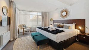 A modern bedroom with a large bed, a chair, a desk, and a TV. - Happy Daze Central Queenstown Hot Tub (Queenstown)