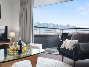 A modern room with a glass table, a sofa, and a view of snow-capped mountains. - Happy Daze Central Queenstown Hot Tub (Queenstown)