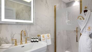 A luxurious bathroom with a white marble sink, gold fixtures, and a glass-enclosed shower.