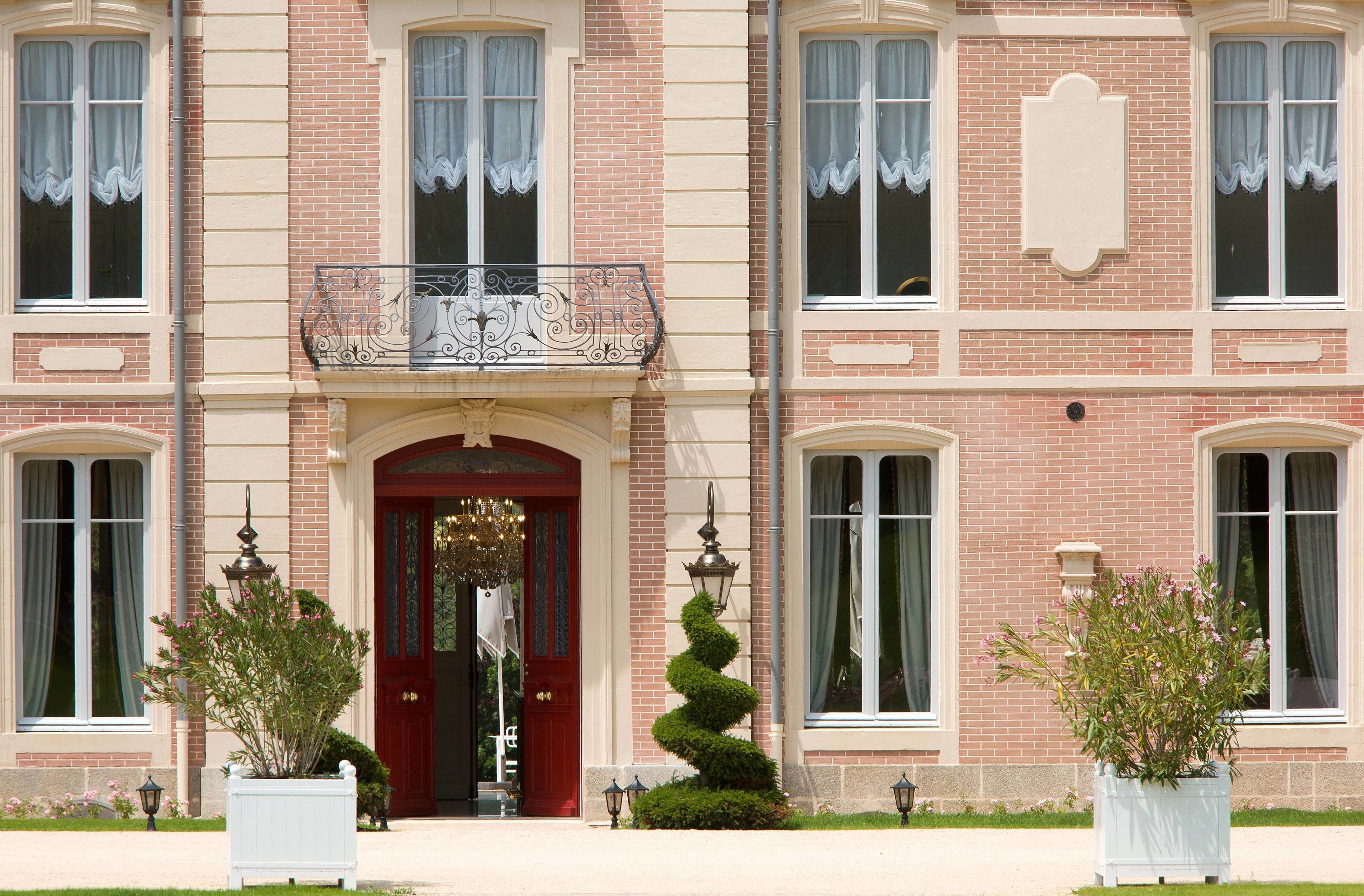 A two-story building with a red entrance door, white-framed windows, and a decorative iron balcony.