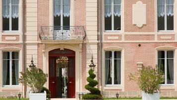 A two-story building with a red entrance door, white-framed windows, and a decorative iron balcony.