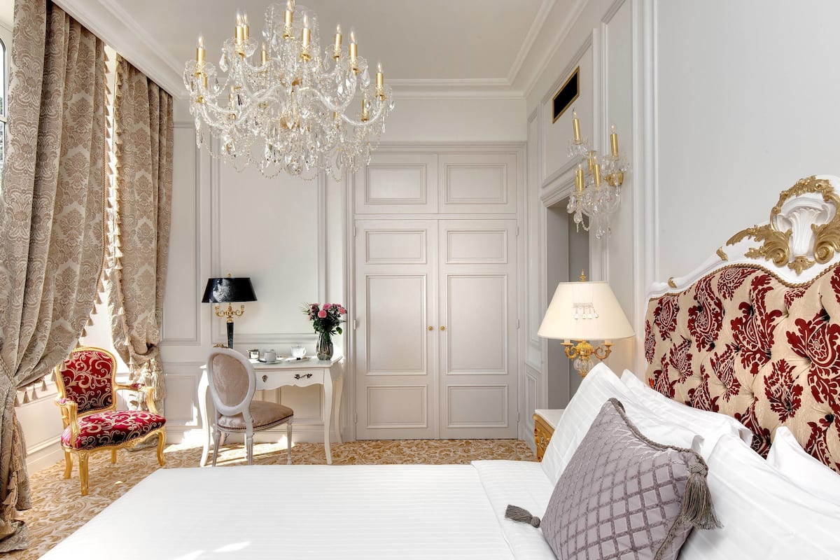 Une chambre d’hôtel avec un grand lit, un bureau, une chaise, un lustre et une armoire.