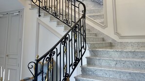 Un magnifique escalier avec une rampe en fer forgé noir, des marches en marbre et un lustre.