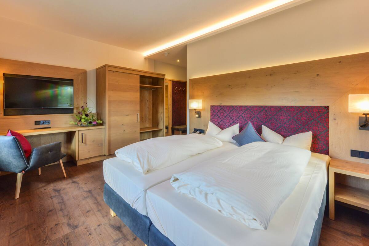 A modern hotel room with a large bed, a desk, a TV, and a wardrobe.