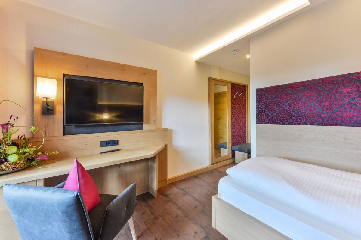 A hotel room with a bed, a desk with a flat-screen TV, a chair, and a mirror.