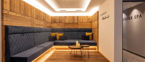Un spa moderno con una pared de madera, un banco acolchado oscuro y una pequeña mesa con velas.