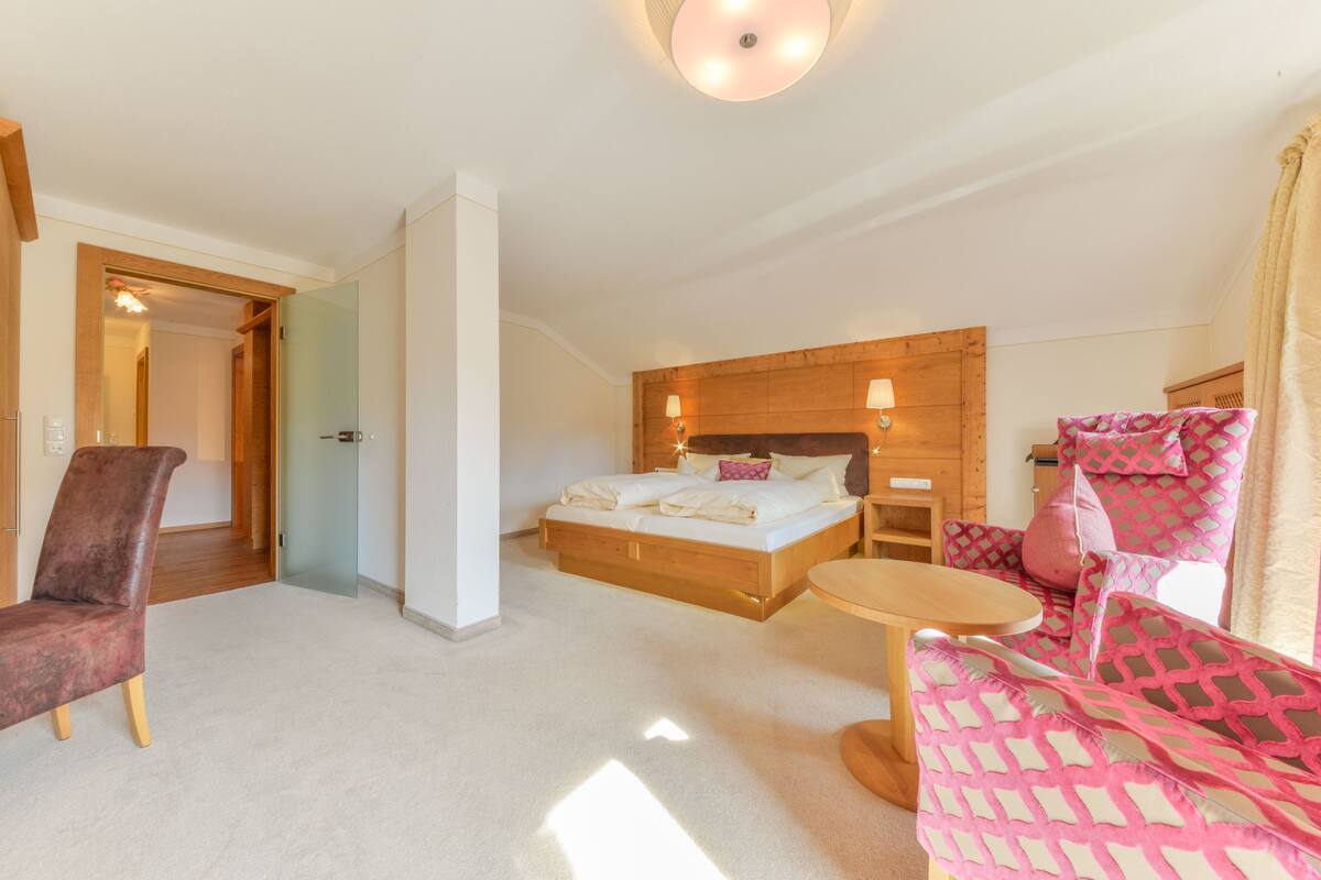 A hotel room with a bed, a chair, a small table, and a wooden headboard.