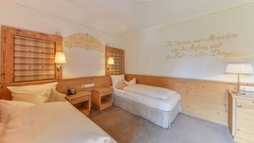 A hotel room with two beds, a wooden headboard, a bedside table with a lamp, a small desk, and a wall with a decorative quote.