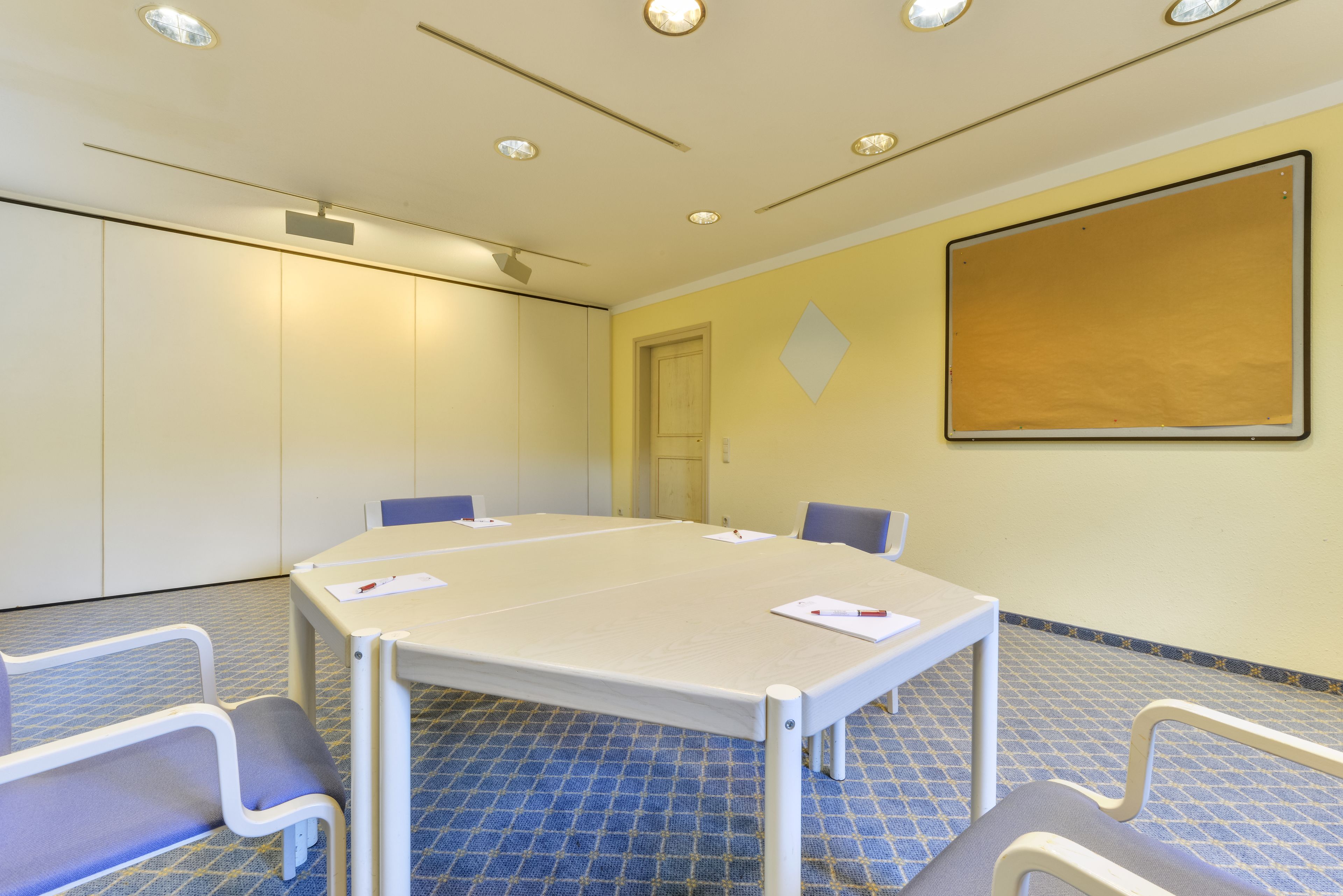 A conference room with a large table, four chairs, a whiteboard, and a patterned floor.