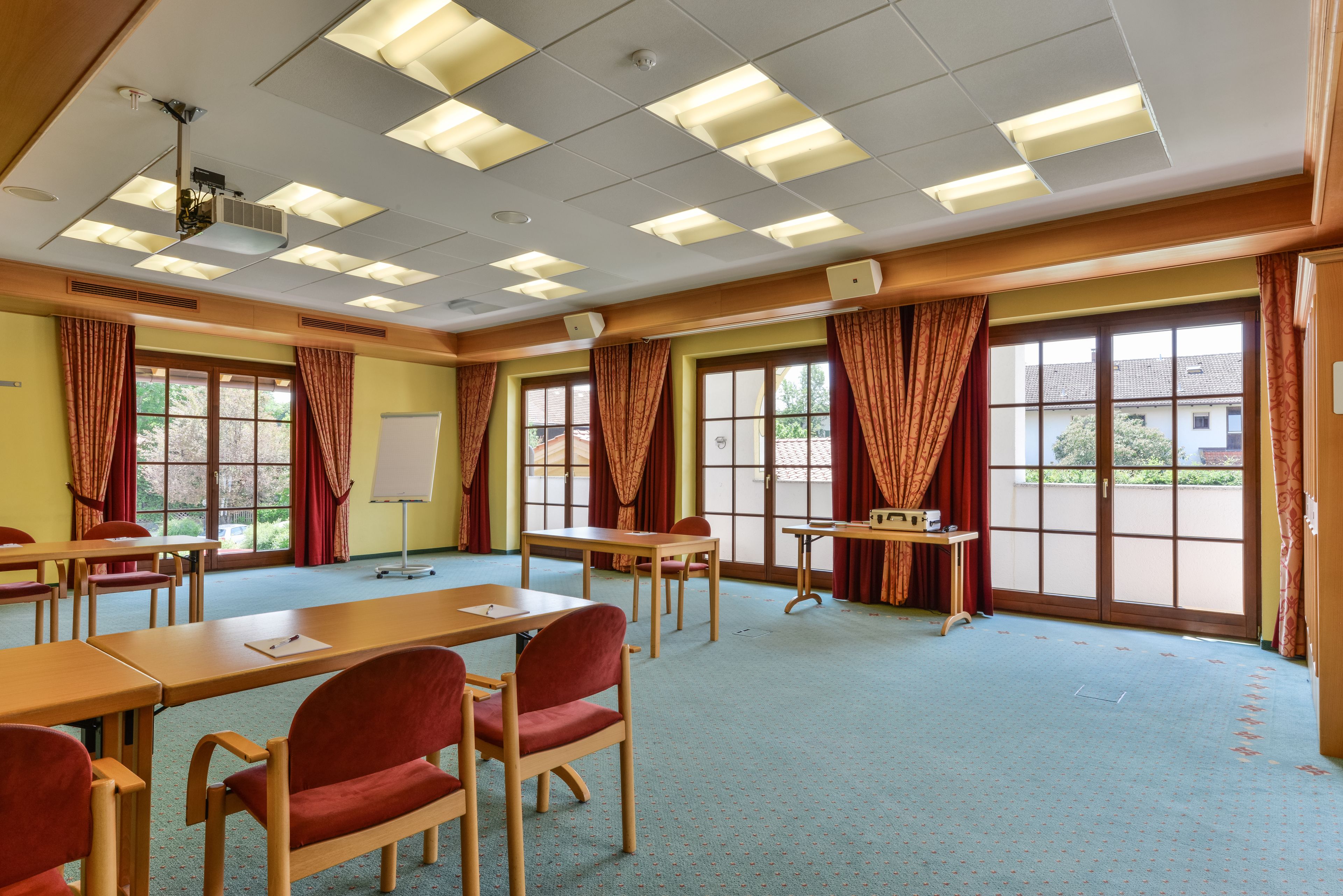 A conference room with tables, chairs, a whiteboard, and large windows with curtains.