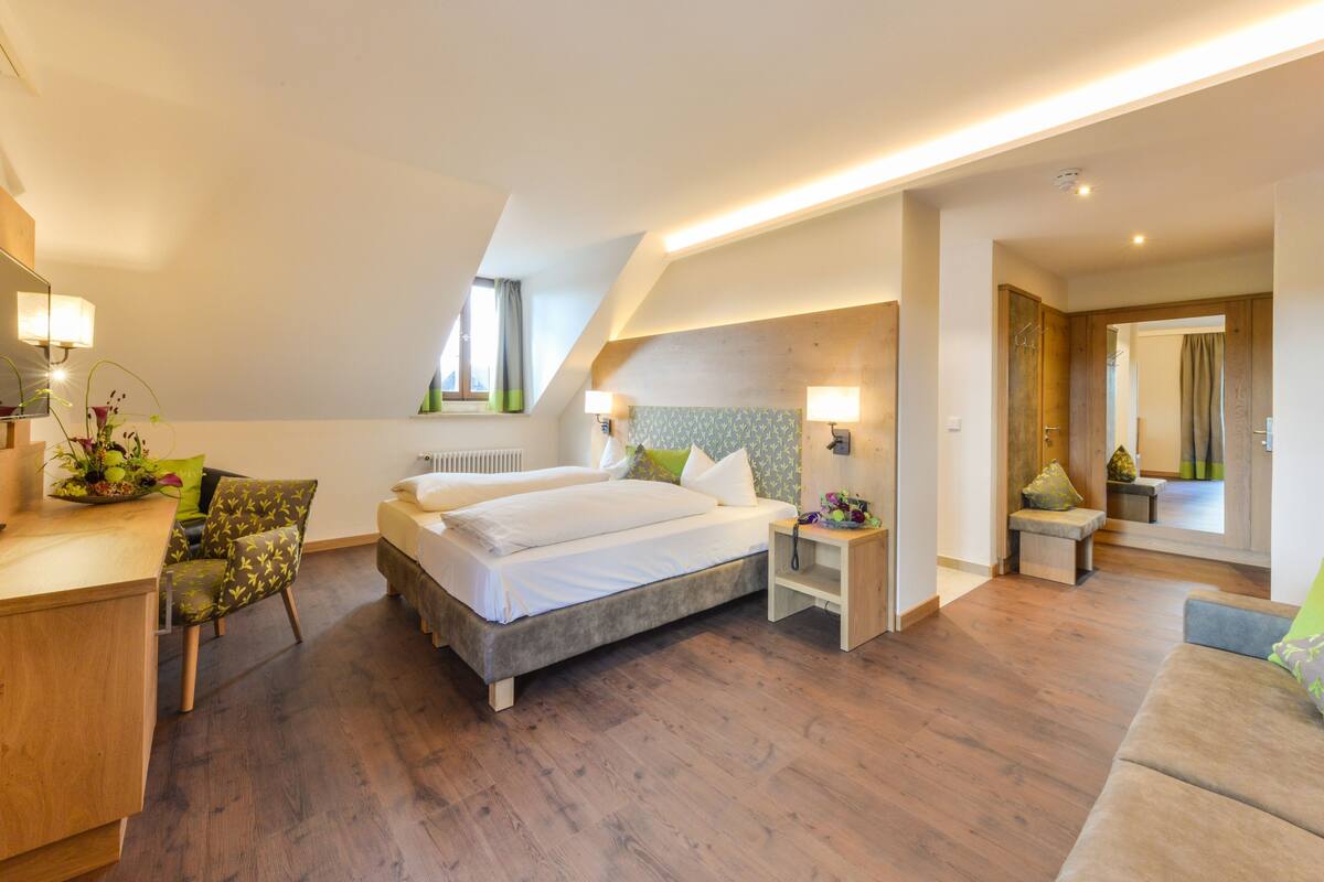 A modern hotel room with a large bed, a desk, a chair, and a sofa.