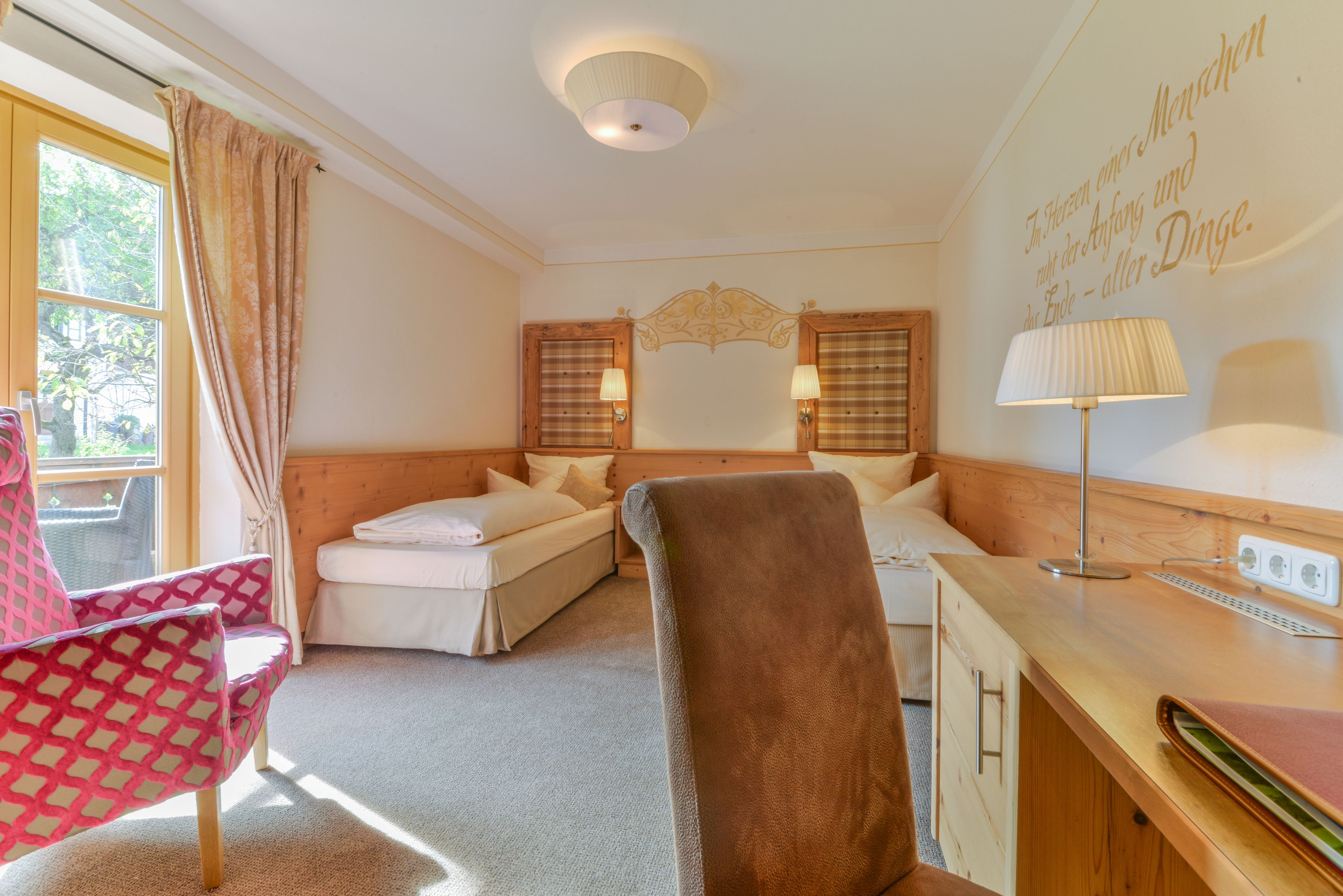 A hotel room with a bed, a desk, a chair, and a window with curtains.