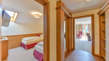 Een slaapkamer met twee bedden, een houten garderobe, een aan de muur bevestigde televisie en een dakraam.
