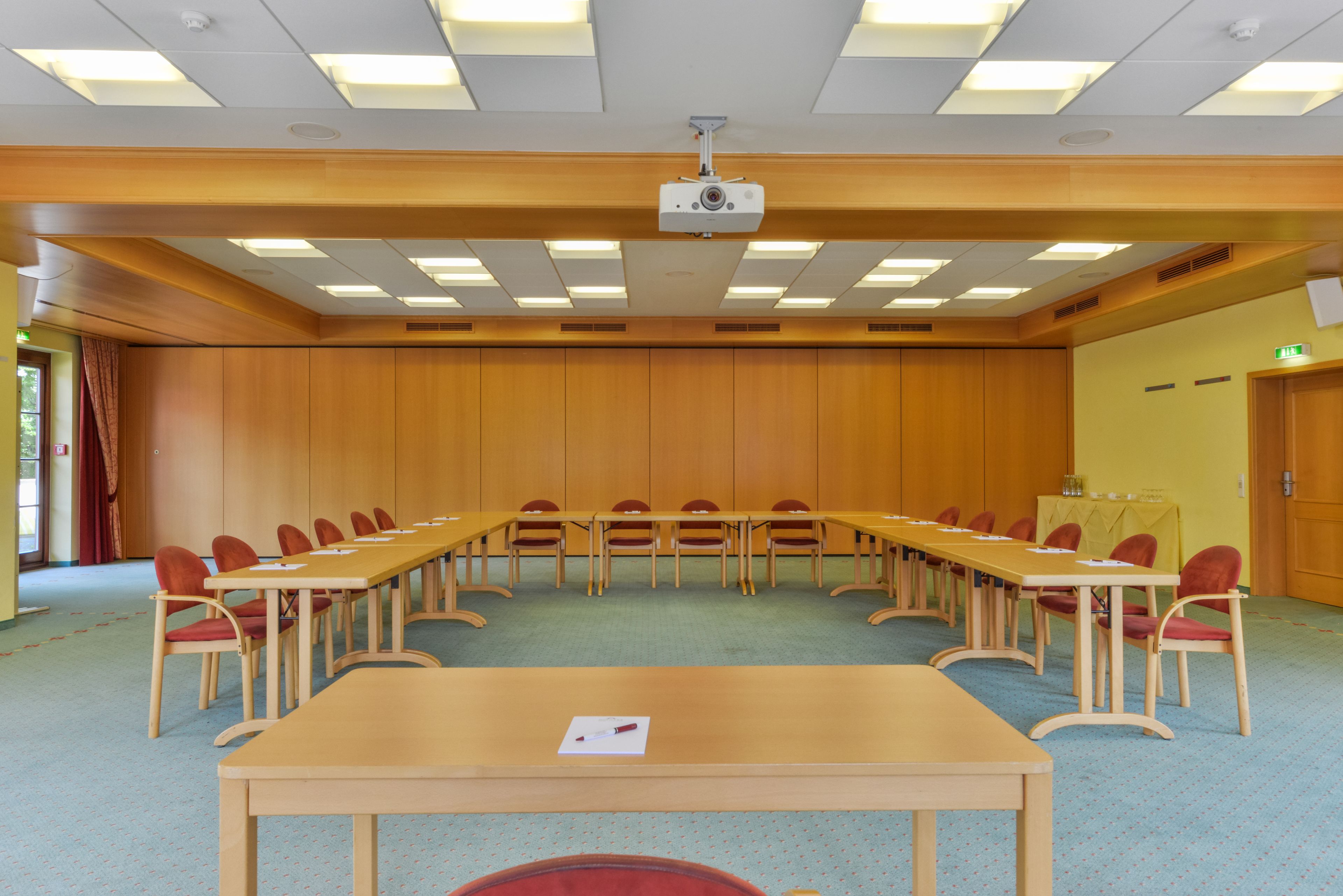 Ein Konferenzraum mit einem langen Tisch, mehreren Stühlen und einem an der Decke befestigten Projektor.