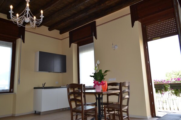 A dining area with a table, chairs, a chandelier, a TV mounted on the wall, and a window with a view of greenery. - Locanda La Sosta (Cavaion Veronese)