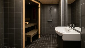 Ein modernes Badezimmer mit dunklen Fliesen, einer Holzbank, einer Dusche und einem weißen Waschbecken.