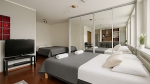 Ein modernes Hotelzimmer mit einem großen Bett, einem Fernseher, einem Spiegel und Blick zur Küche.