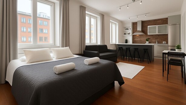 Ein modernes Hotelzimmer mit einem großen Bett, einer Sitzecke, einer Küchenzeile und Blick auf ein rotes Gebäude.