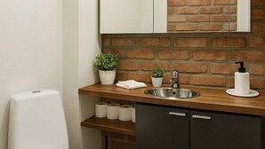 Ein modernes Badezimmer mit Backsteinwand, Toilette in Weiß, Waschbecken inklusive Spiegel und einem kleinen Topfpflanzen.