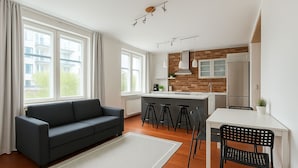 Ein modernes Apartment mit Sofa, Esstisch, Küche und großen Fenstern.