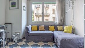 A room with a checkered floor, a grey sofa with yellow cushions, a standing fan, and a window with a view of buildings. - Venezia - Lido Erizzo 15 (Venice)