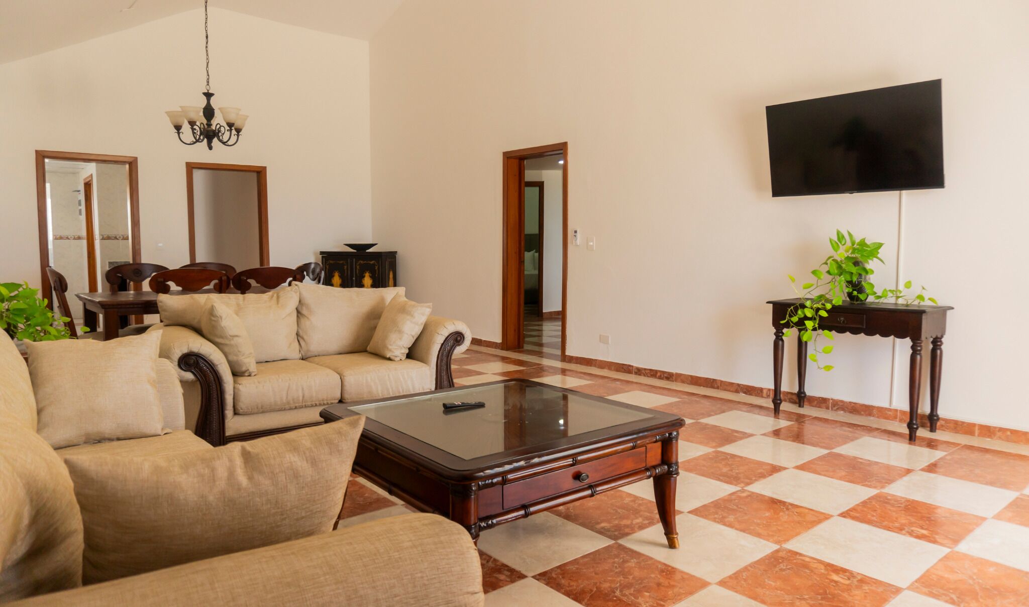 Una sala de estar con un sofá, sillones, una mesa de centro, un televisor y una planta.