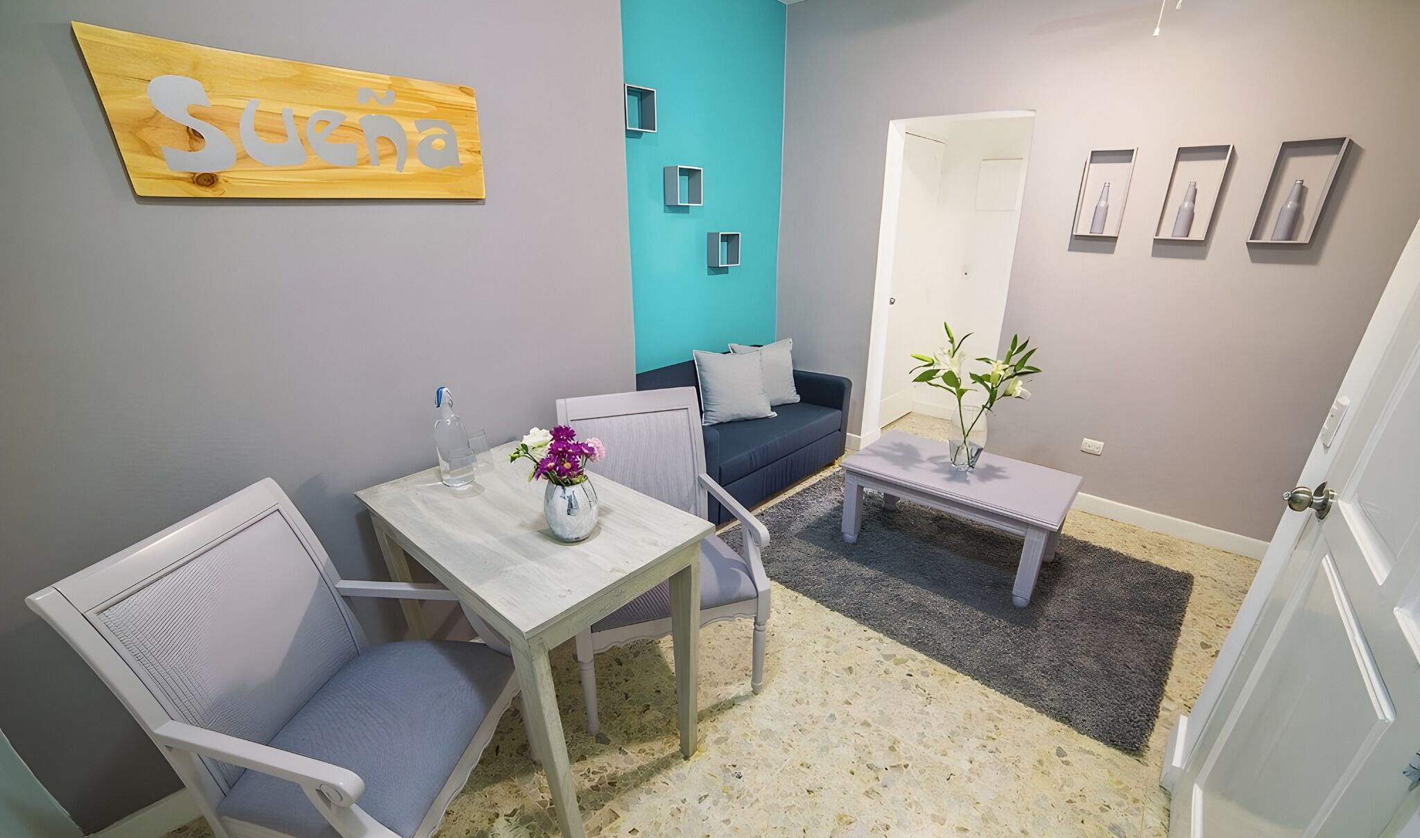 Una sala de estar moderna con un sofá, una mesa de comedor con sillas, una pequeña mesa de centro y un letrero en la pared.