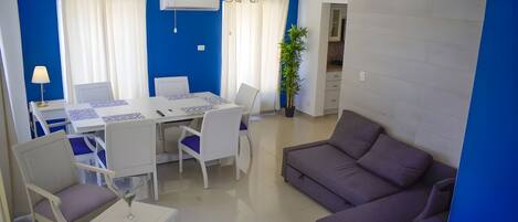 A modern living room with a dining area, featuring a sofa, chairs, a table, and a potted plant.