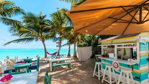 A beachside café with outdoor seating, a colorful food stand, and a clear view of the ocean. - Hotel Checkin El Cortecito Beach (Punta Cana)