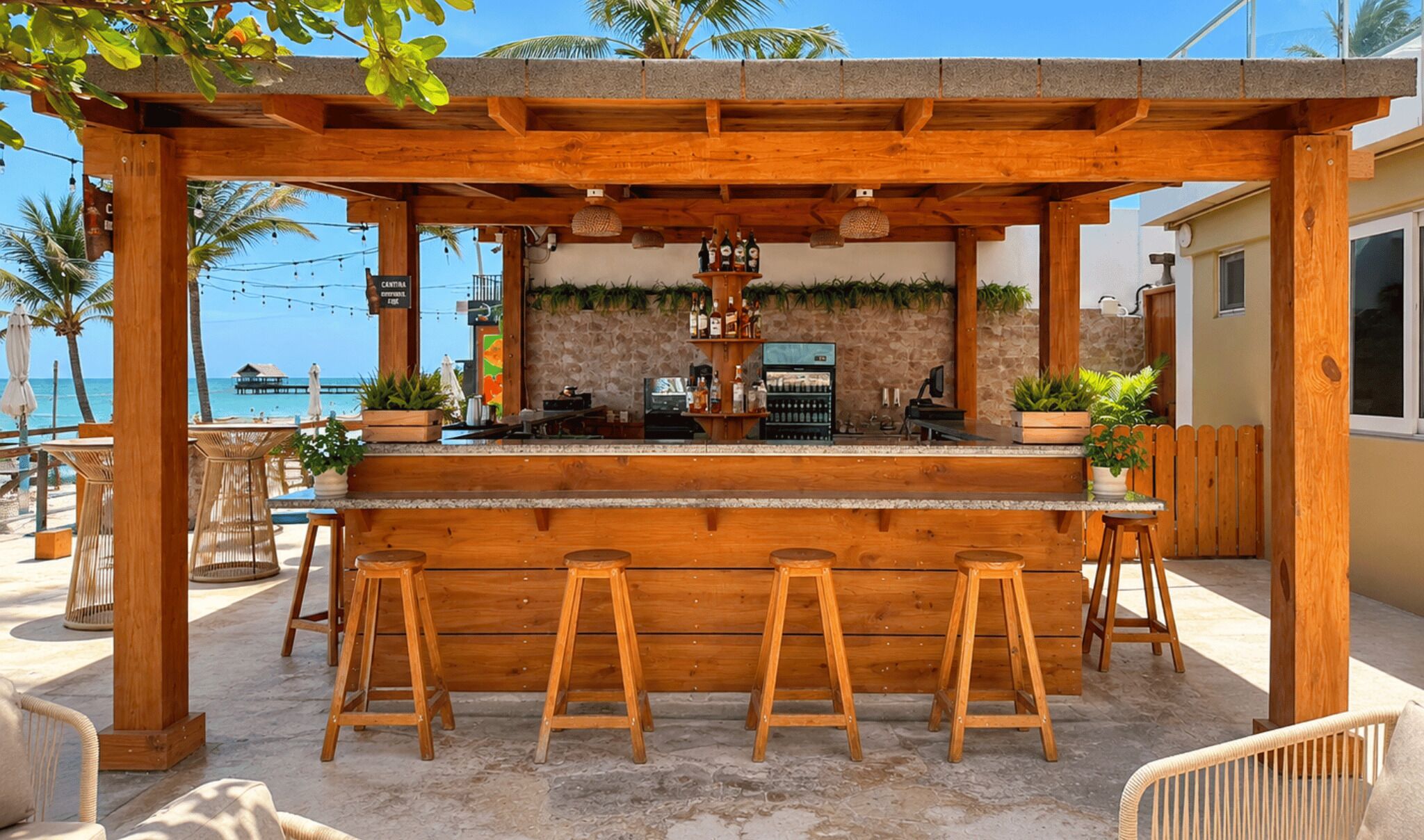 A wooden bar with stools, a stone wall, and a view of the beach.