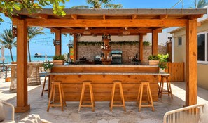 A wooden bar with stools, a stone wall, and a view of the beach. - Hotel Checkin El Cortecito Beach (Punta Cana)