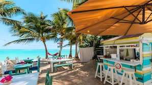 Un café frente a la playa con terraza, un puesto de comida llamativo y vista despejada al océano.