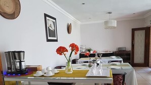 A dining area with a glass table, white chairs, and a coffee machine. - Four Seasons Lehae Guest House (Sandton)