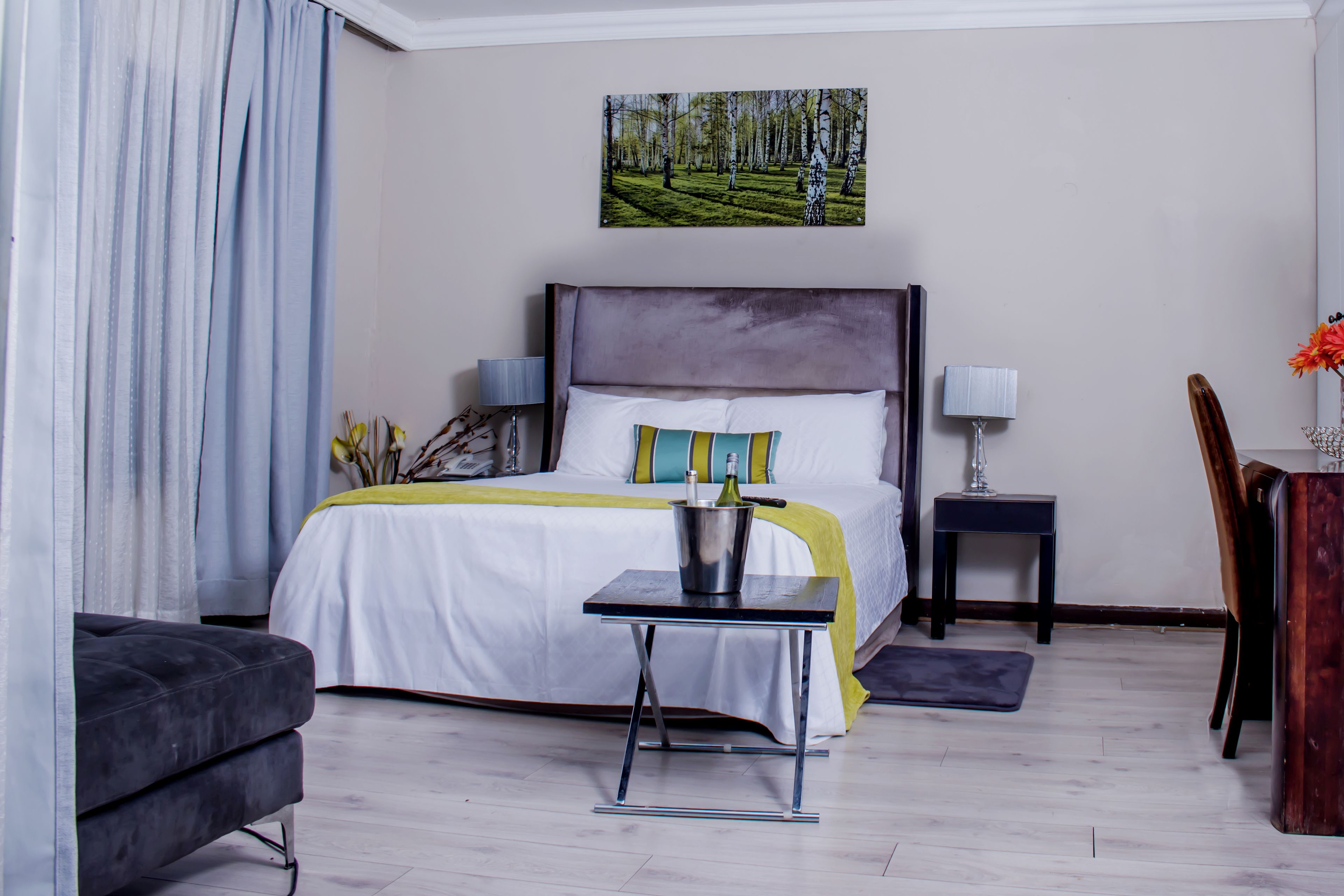 Une chambre à coucher avec un lit, des tables de chevet, une petite table, une chaise et un tableau accroché au mur.