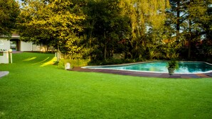 A well-maintained lawn with a swimming pool, surrounded by trees and a house. - Four Seasons Lehae Guest House (Sandton)