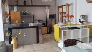 A modern kitchen with a central island, a dining area with a glass table, and a living space with a sofa. - Four Seasons Lehae Guest House (Sandton)