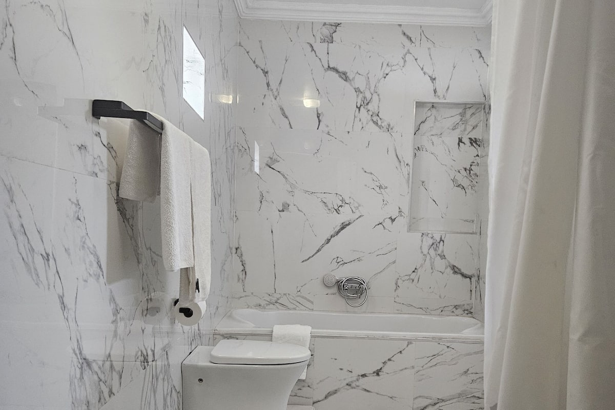 Une salle de bain comprenant des toilettes, un lavabo et une baignoire, le tout agrémenté de murs en marbre.