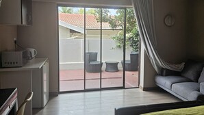 A hotel room with a bed, a desk with a microwave, a chair, and a view of the outside patio. - Four Seasons Lehae Guest House (Sandton)