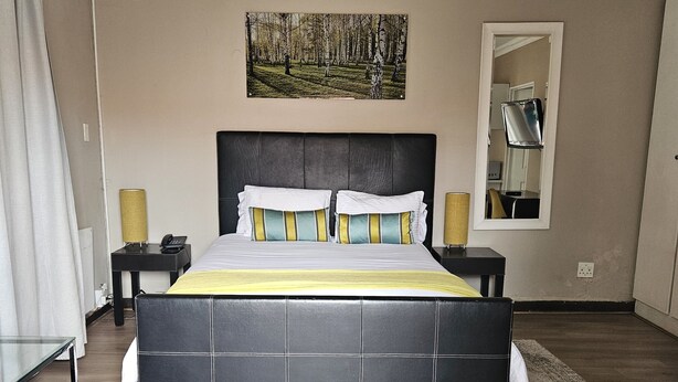 A bedroom with a large bed, two bedside tables, a mirror, and a painting on the wall. - Four Seasons Lehae Guest House (Sandton)