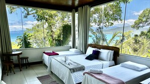 Ein Hotelzimmer mit zwei Betten, einem kleinen Tisch und Blick auf das Meer und die Berge.